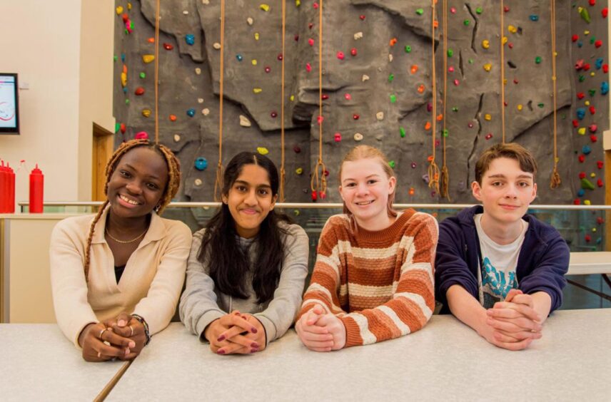 Children sitting in front of a climbing wall.