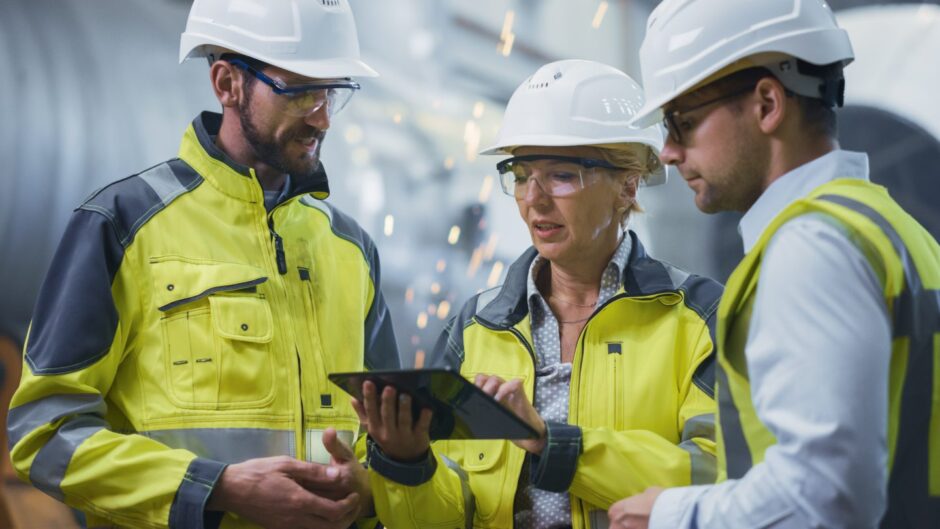 two male and one female engineer look at a laptop