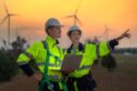 two workers at a wind facility talk while holding a laptop, showing the digital transformation in the energy sector