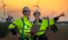 two workers at a wind facility talk while holding a laptop, showing the digital transformation in the energy sector