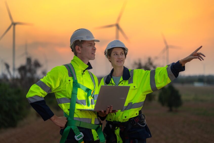 two workers at a wind facility talk while holding a laptop, showing the digital transformation in the energy sector