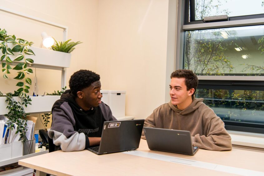 two ISA students sit at a table with their laptops 