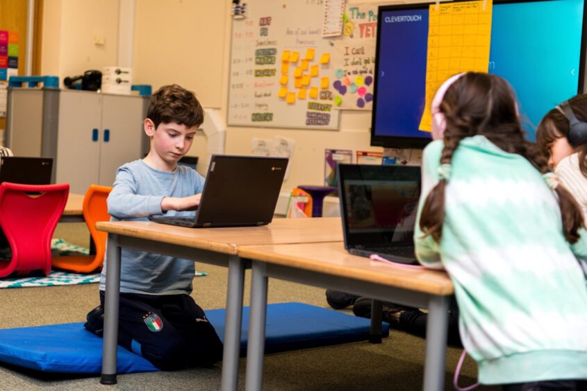 young students sit on the floor around tables with their laptops