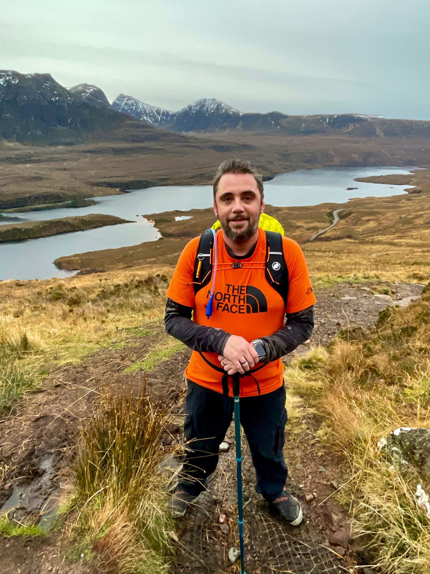 Allan Basil wearing hiking gear and standing on a trail in the Scottish Highlands.