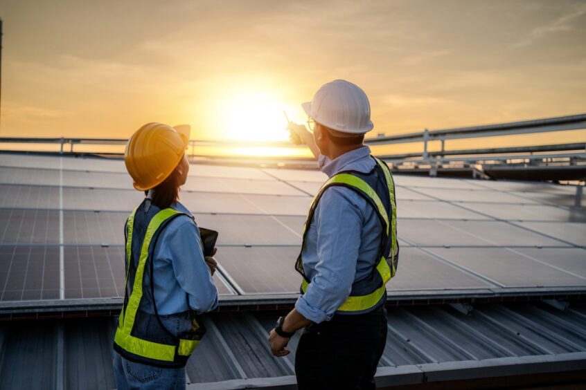 Engineers look at sun in the horizon after installing solar panels, increasing renewable energy capacity as reported in DNV UK ETO