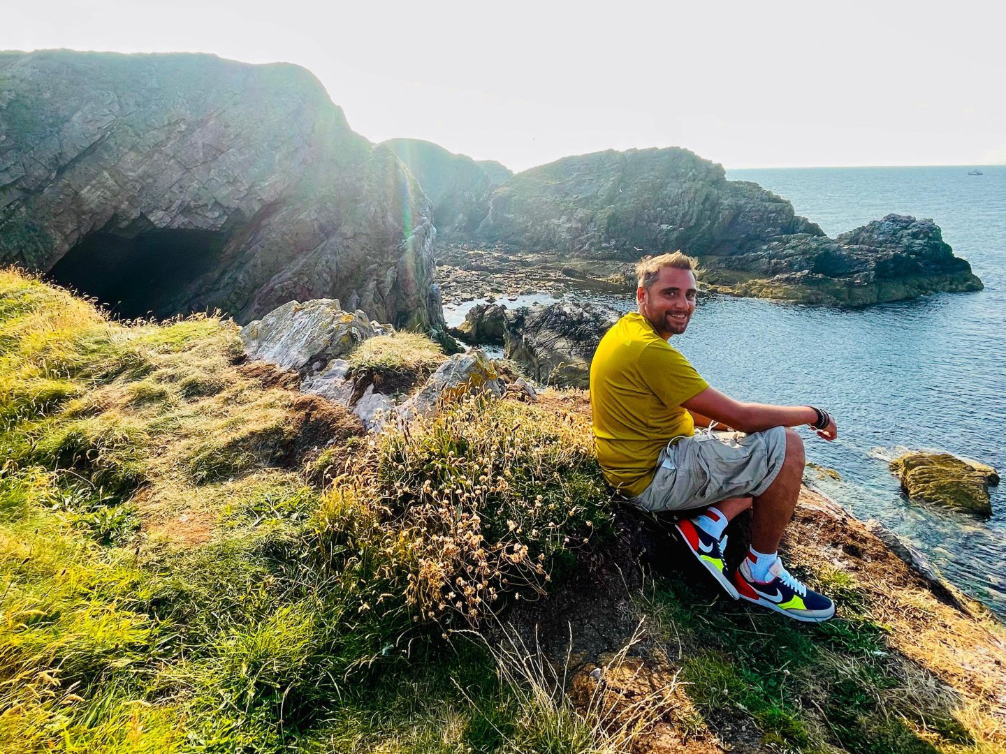 Allan Basil pictured sitting near the edge of a cliff overlooking the sea. 