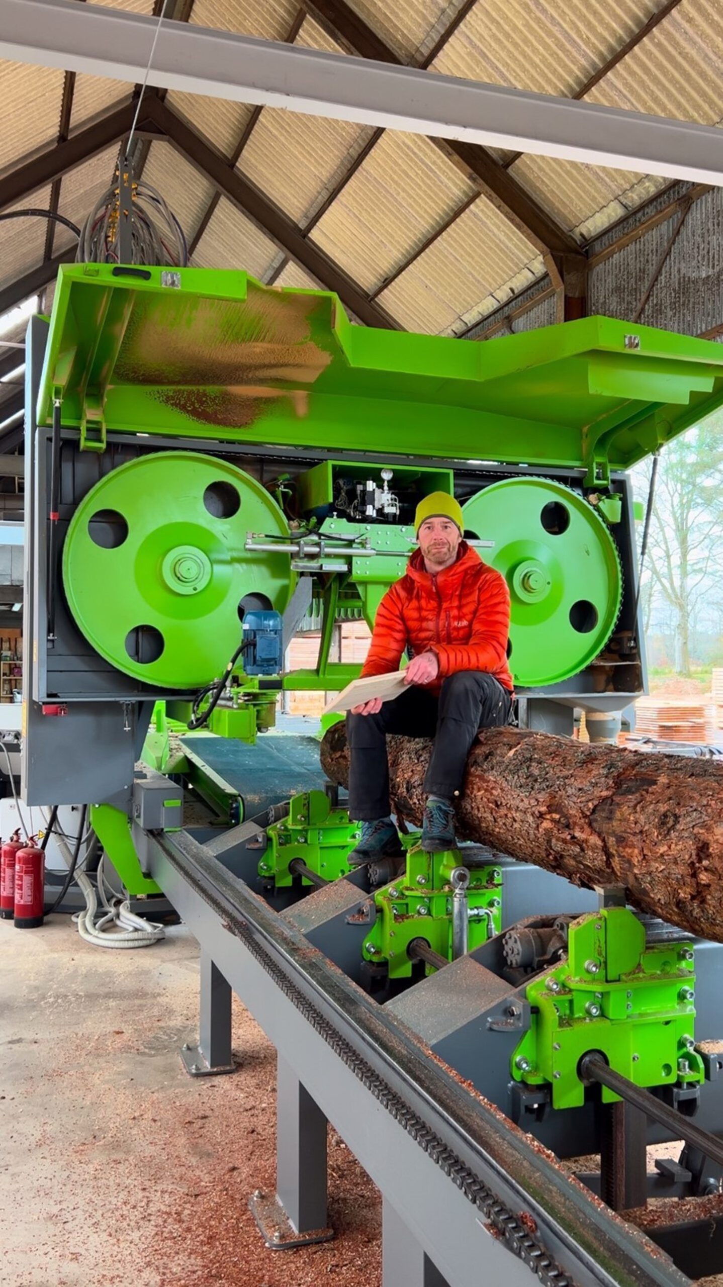 Guy Phillips sitting on a piece of timber next to a large piece of wood working machinery.