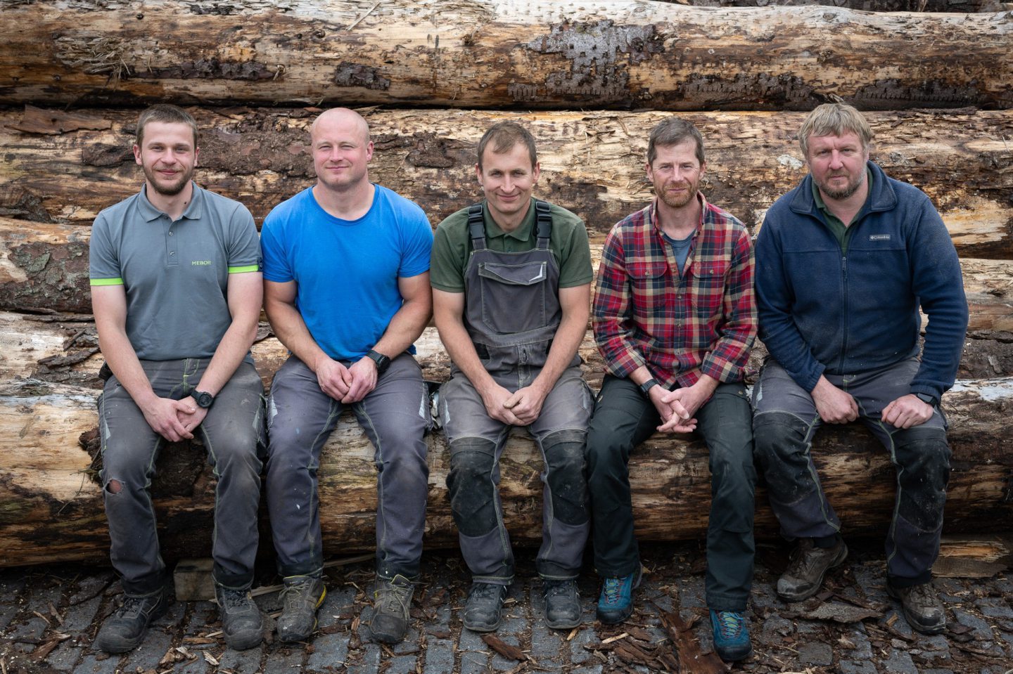 Highland Heritage Woodworks team members Alvis Krasovskis, Jurgis Baltmanis, Arturs Zommers, Guy Phillips and Armands Balams sitting on a pile of timber.