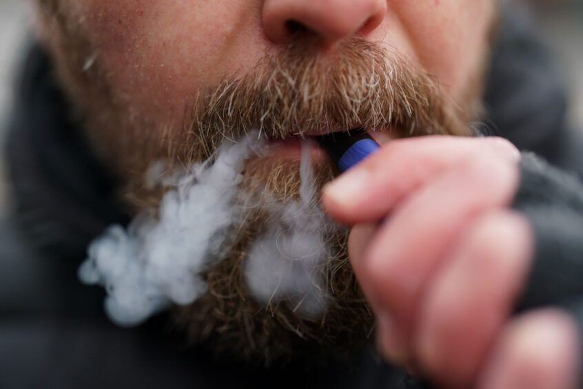 A close up shot of a man with a beard vaping.