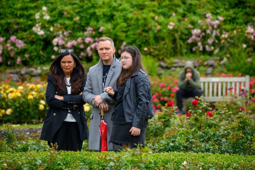 Three people stand solemnly in the North Sea Memorial Garden in Aberdeen during the Piper Alpha 2025 remembrance event.