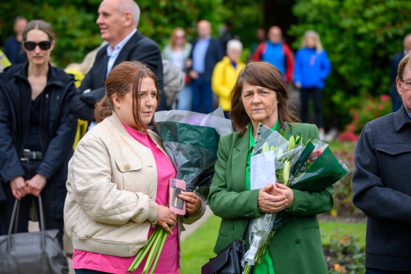 Two women hold bouquets while attending the 2025 Piper Alpha memorial service at Hazlehead Park in Aberdeen.