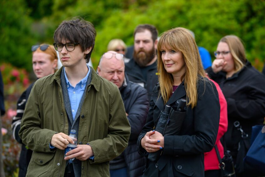 Crowd of attendees stand in reflection during the 2025 Piper Alpha remembrance event at Hazlehead Park, Aberdeen.