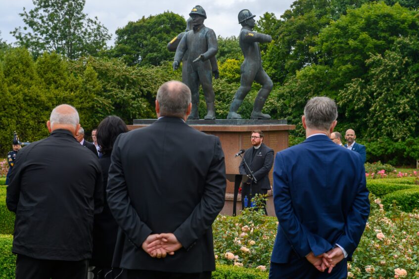 Chaplain Michael Mair speaks at a podium during the 2025 Piper Alpha memorial service in front of the North Sea statue in Aberdeen.