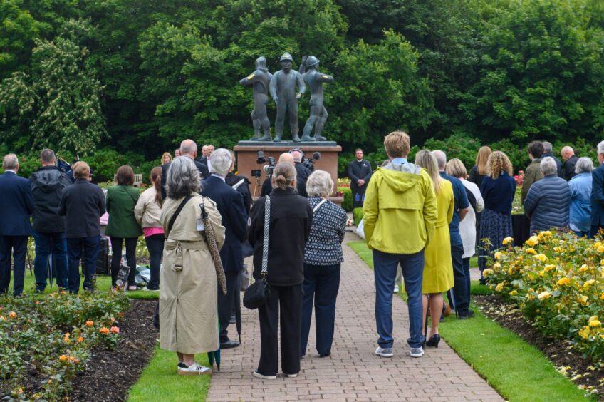 Crowd stands facing the Piper Alpha memorial statue during the 2025 remembrance service in Hazlehead Park, Aberdeen.
