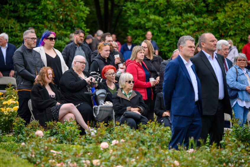 Crowd of people, some seated and others standing, observe the 2025 Piper Alpha memorial ceremony in Hazlehead Park, Aberdeen.