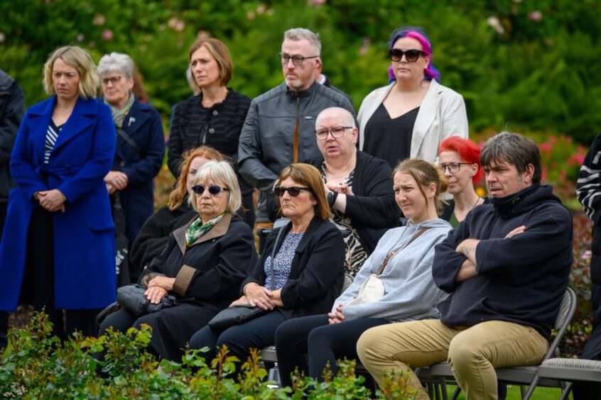 A group of people seated and standing in reflective silence during the 2025 Piper Alpha memorial service at Hazlehead Park, Aberdeen.