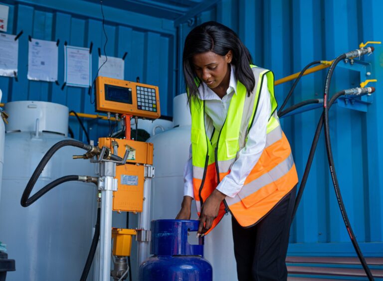 A young Black woman, dressed in professional attire, is filling liquefied petroleum gas into a client's tank at a filling station