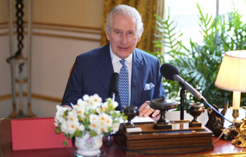 King Charles, wearing a blue suit, sits behind a desk, for our health benefits of friendship article.