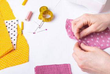 Woman's hands sewing pink fabric with scattered yellow fabric and pins