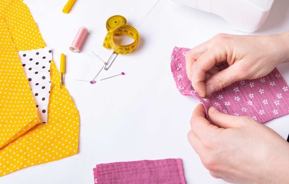 Woman's hands sewing pink fabric with scattered yellow fabric and pins