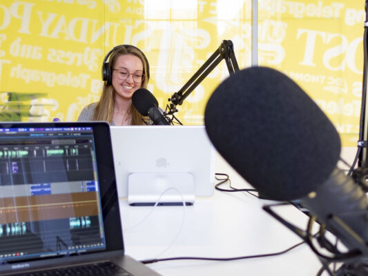 Abbie at podcast studio with editing screen and mic in foreground