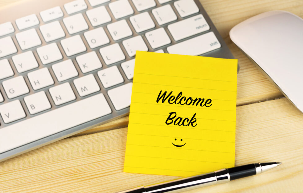 Welcome Back sticky note on desk with keyboard and mouse