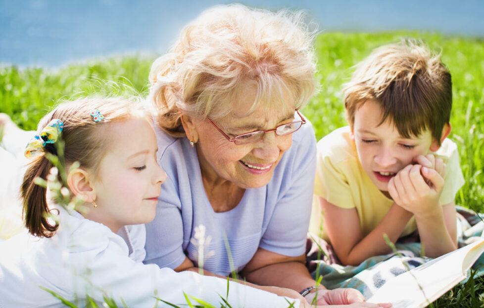 Grandparent reading to children on grass