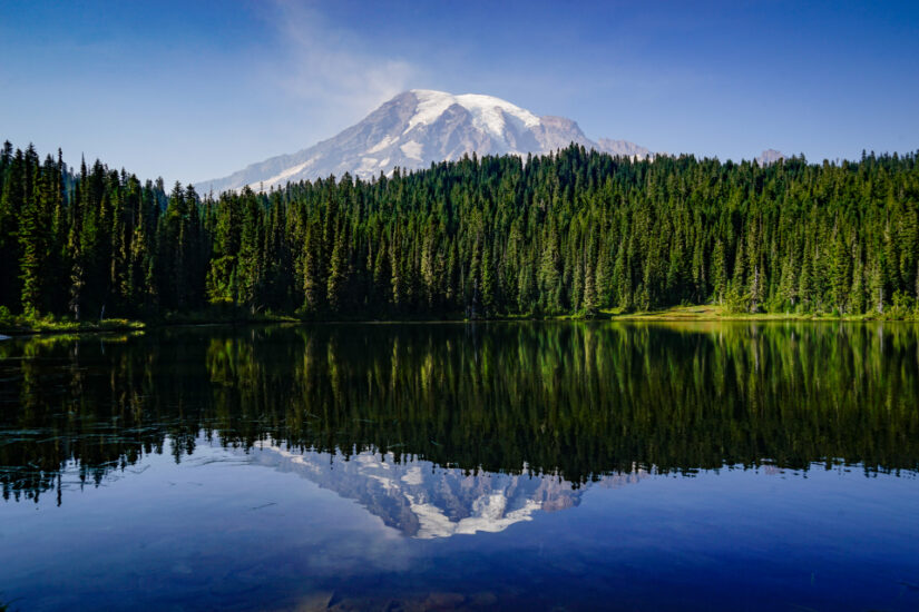 ‘Mount Rainier’. A mountain rests on top of a sea of green trees, with its reflection caught in the crisp blue water. By Nicole Schwamb, taken in Washington, USA. Provided by The CEWE Photo Award.
