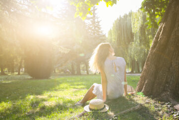 Woman sitting under tree with sun glaring