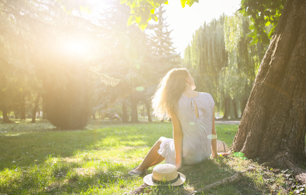 Woman sitting under tree with sun glaring