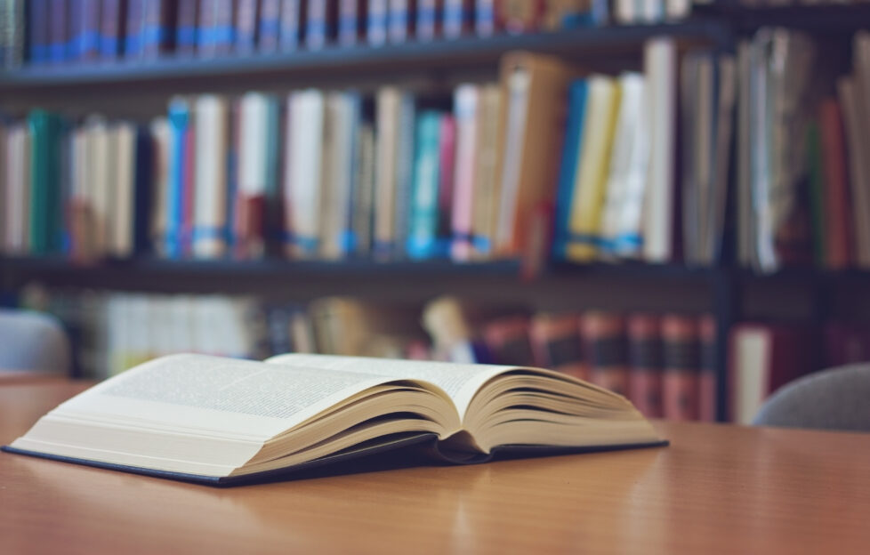 Book lying open on a table with bookshelf in the background