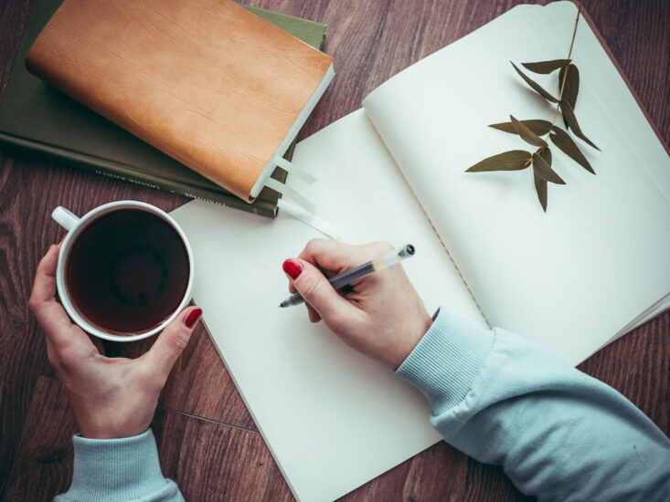 Woman's hand writing in blank notebook with a coffee
