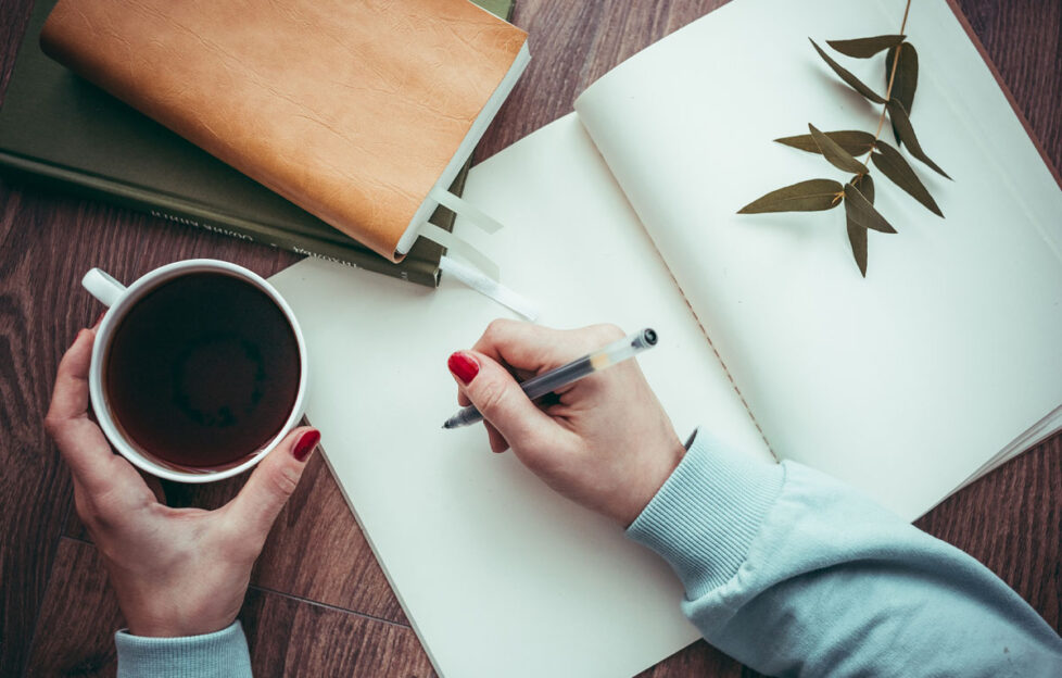 Woman's hand writing in blank notebook with a coffee