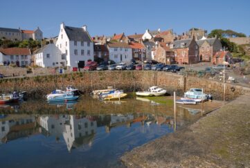 View of Crail Harbour with docked boats and houses under blue skies