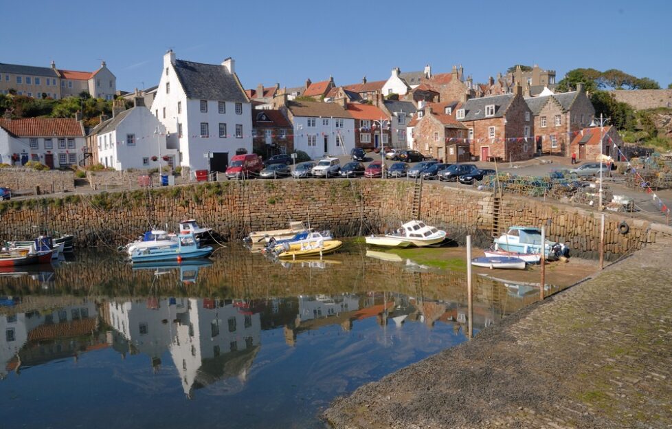 View of Crail Harbour with docked boats and houses under blue skies