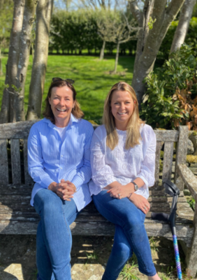 Amelia and Clare, Cool Crutches co founders, sitting on a park bench smiling