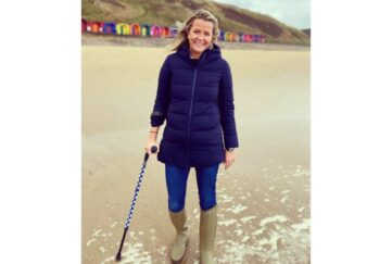 Amelia from Cool Crutches dressed in waterproof coat and wellies with a Cool Crutches walking stick on the beach