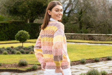 Model wearing knitted striped sweater smiling in front of gardens