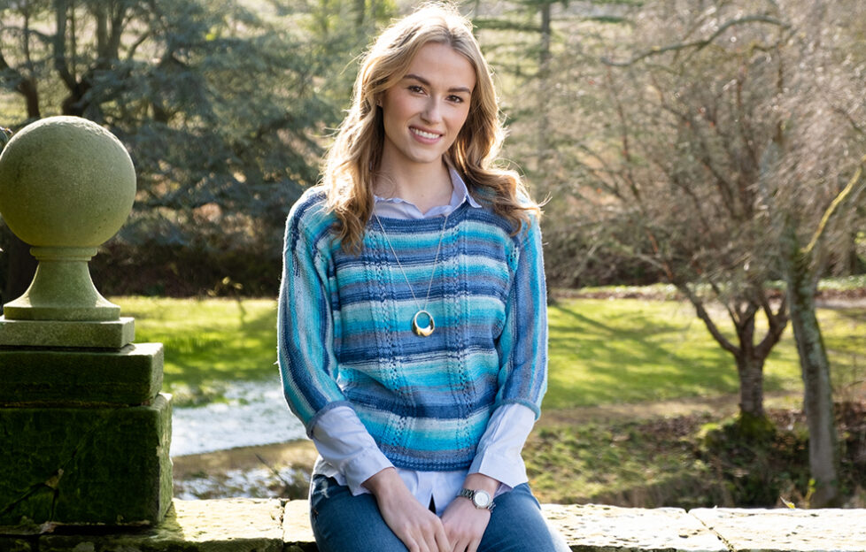 June 25 Knitting Preview: model wearing blue striped knitted top, park in background