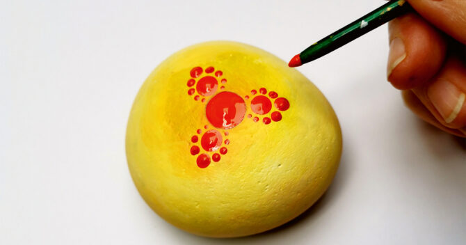 Start of mandala painting stones, red paint on yellow stone, close up