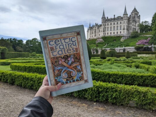 Celtic Fairytales secondhand book held in front of Dunrobin Castle and gardens