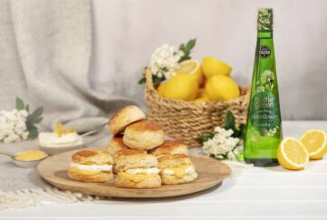 A plate of lemon and elderflower scones, with a basket of lemons and bottle of Bottle Green