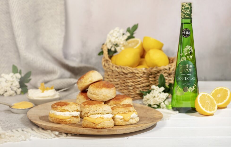 A plate of lemon and elderflower scones, with a basket of lemons and bottle of Bottle Green