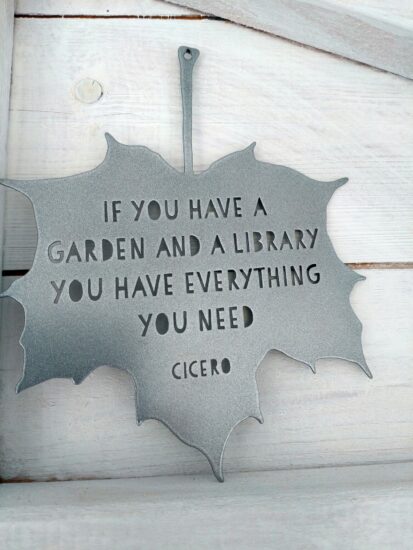 A metal silver hanging ornament in the shape of a leaf reading 'If you have a garden and a library you have everything you need', Cicero quote