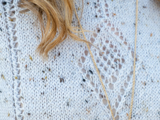 Close up of knitted diamond pattern in close up of knitted diamond top with golden chain necklace