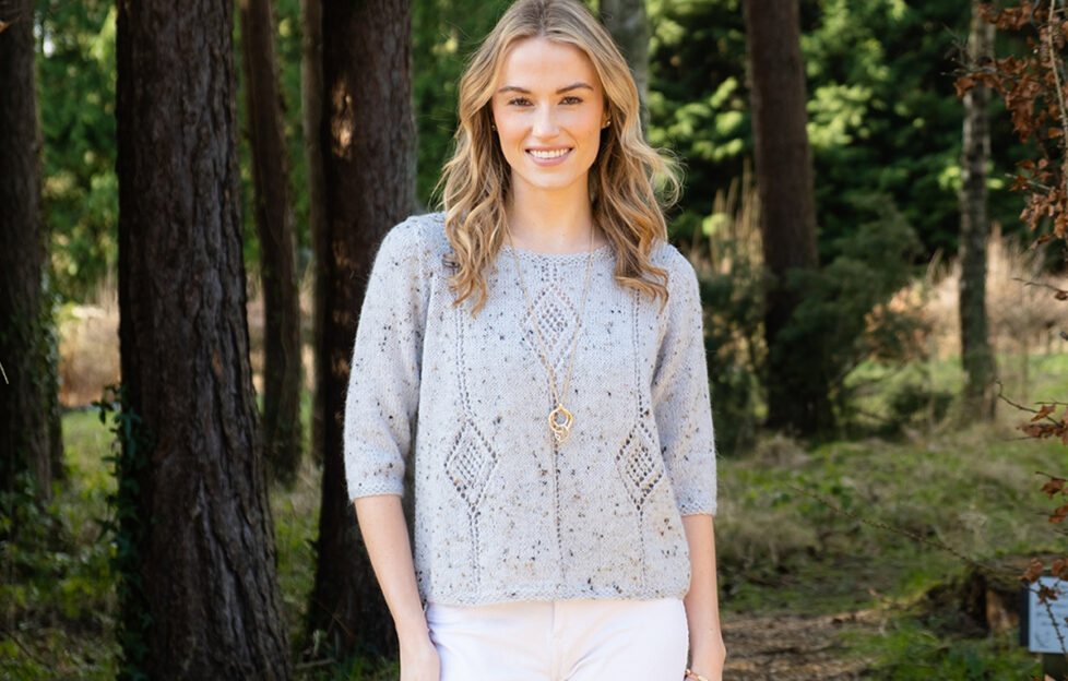 Model wearing knitted diamond top in a wooded area