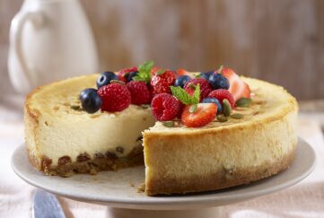 New York Baked Cheesecake topped with strawberries and blueberries on cake stand