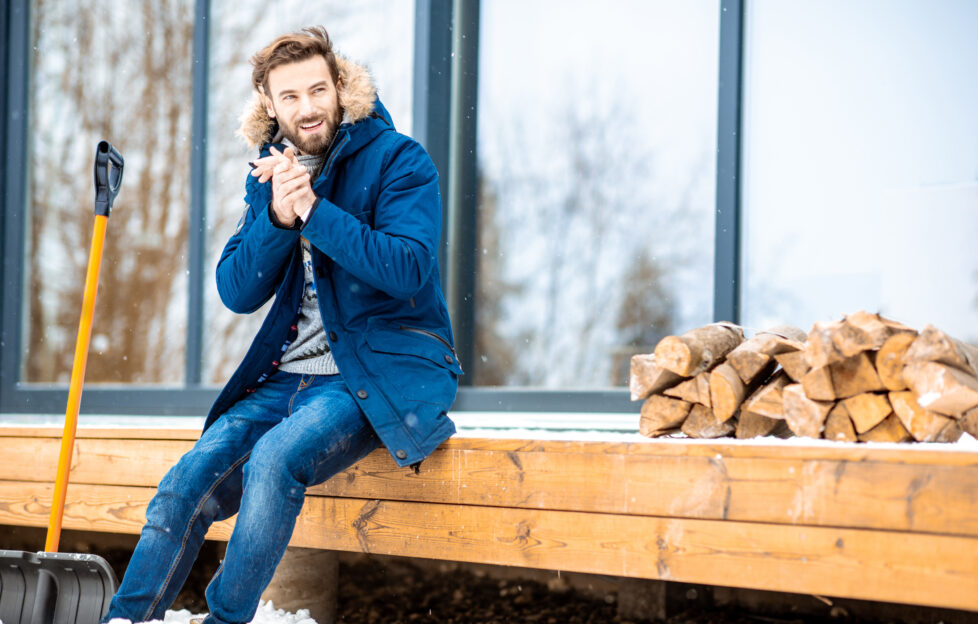 Man sitting on bench in a parka coat rubbing hands together in the cold