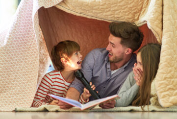 Boy and a father reading books under a blanket fort