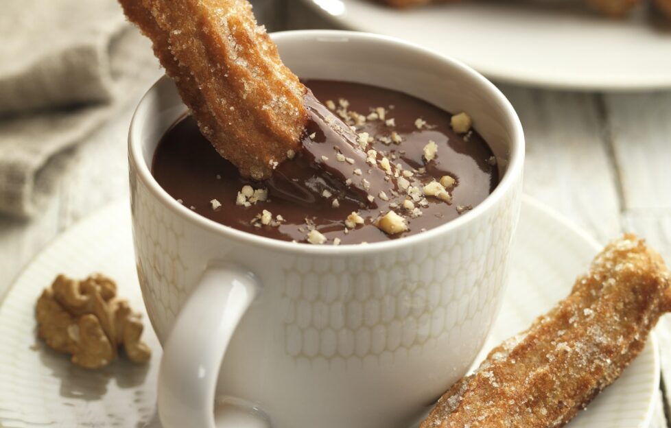 Spanish churros dipped in mug of walnut chocolate